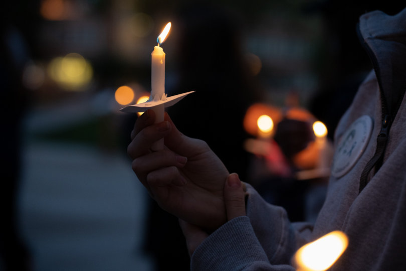 A Remembrance Scholar holds a lit candle by the Remembrance Wall.
