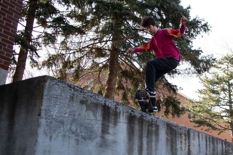 A student does a skateboard trip off of a ledge.