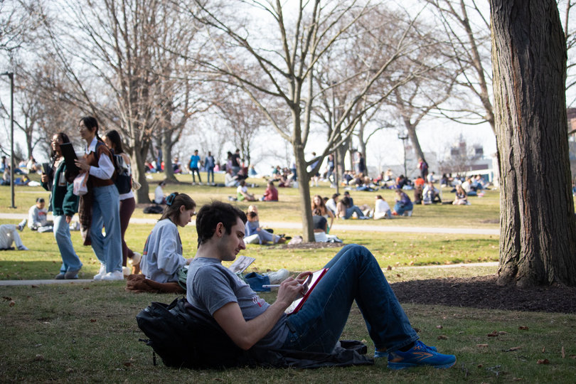 A student works on their iPad while sitting on grass with many other people.
