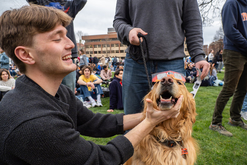 A man puts solar eclipse glasses on a dog.
