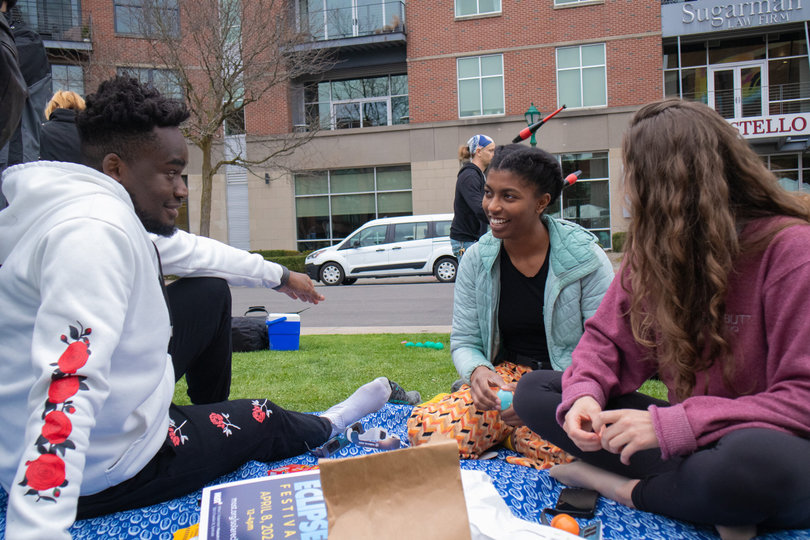 A group of people sit on a blanket.