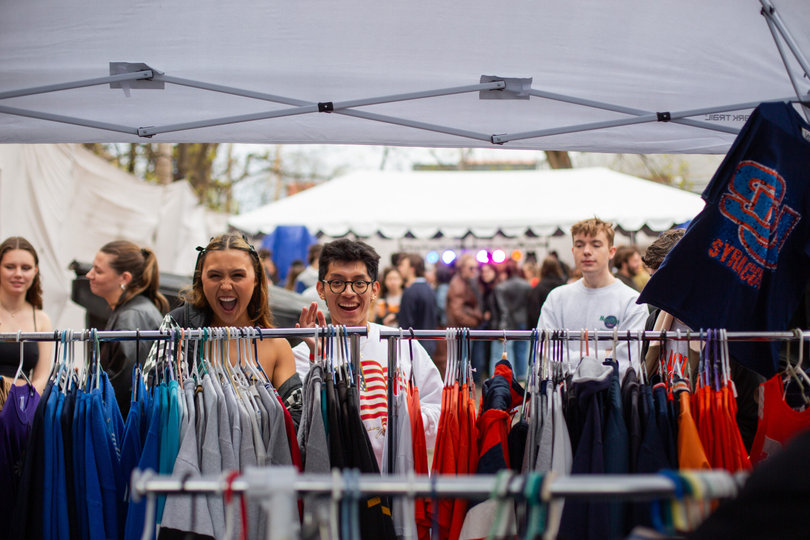 Students smiling into the camera behind clothing racks