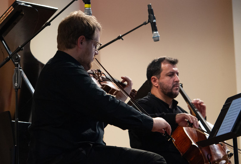 A person playing a violin, another person playing the cello.