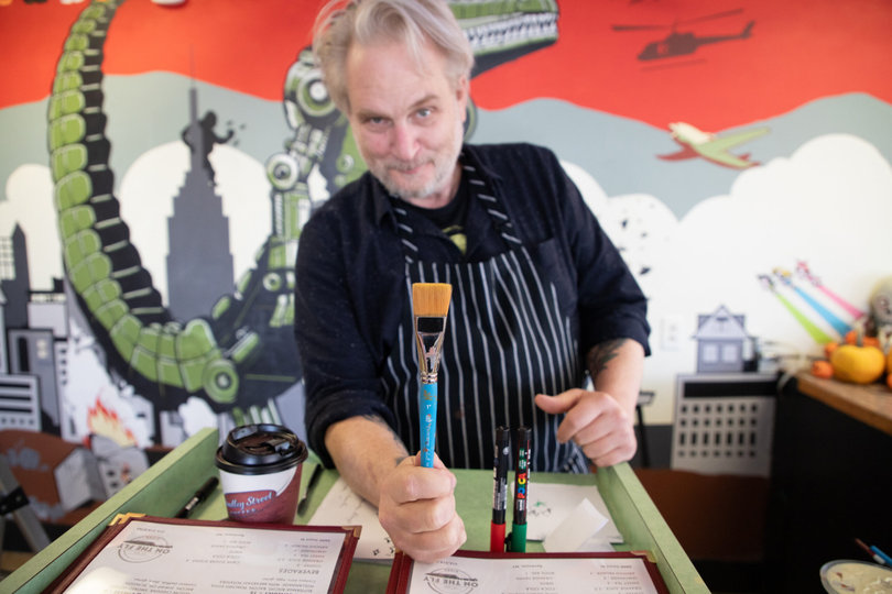 John hand-paints On the Fly’s mural. It depicts a sci-fi scene combining the Seattle, New Orleans and Syracuse skylines.

