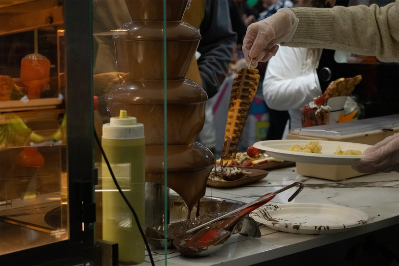 “Chocolate Treats” dips waffles and crêpes in a chocolate fountain displayed in their booth. Treats are decorated with fruits, nuts, rainbow sprinkles, and marshmallows.