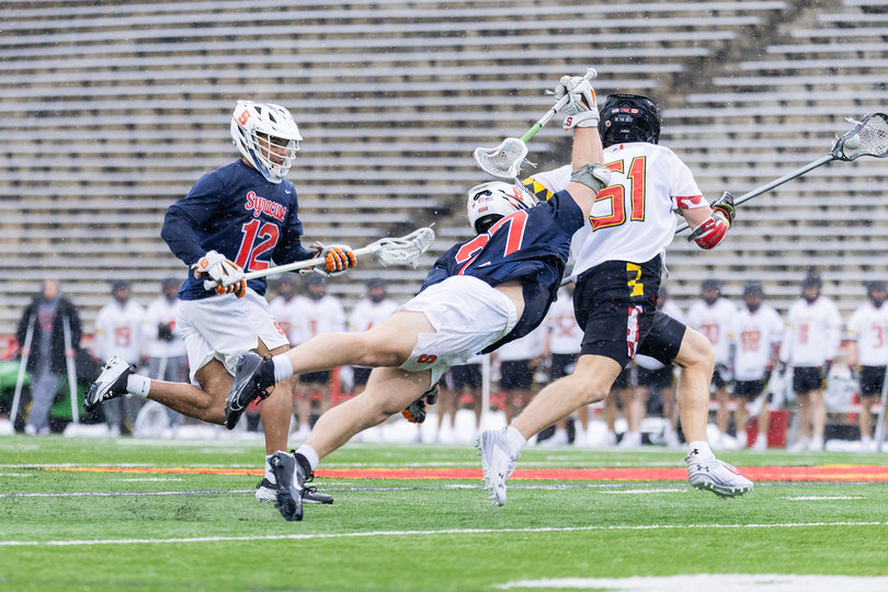 SU faceoff man John Mullen (pictured, No. 27) dives, fully extending his body while rearing his stick back to poke the ball from the stick of Maryland’s Jack McDonald (pictured, No. 51). McDonald picked up a game-high seven ground balls to help the Terrapins control time of possession over the Orange. 