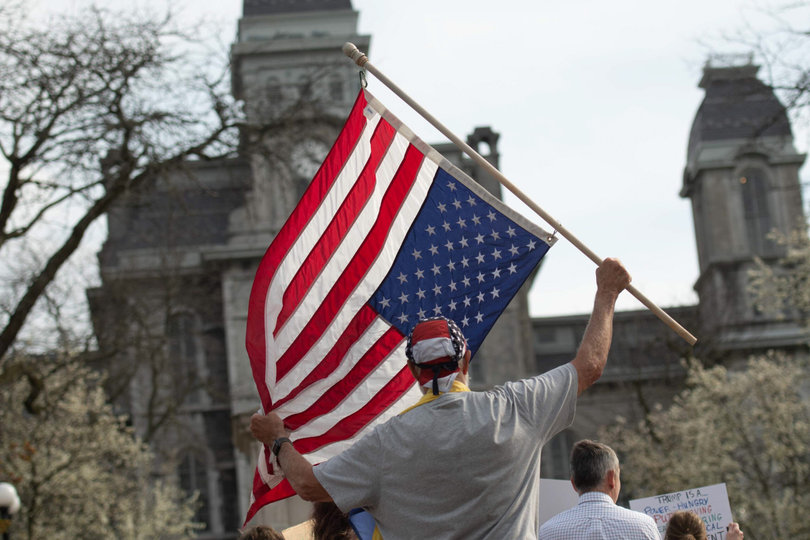 A protester waves an upside-down American flag, a symbol for distress in the country. The rally came just over three months after President Donald Trump took office for a second time.