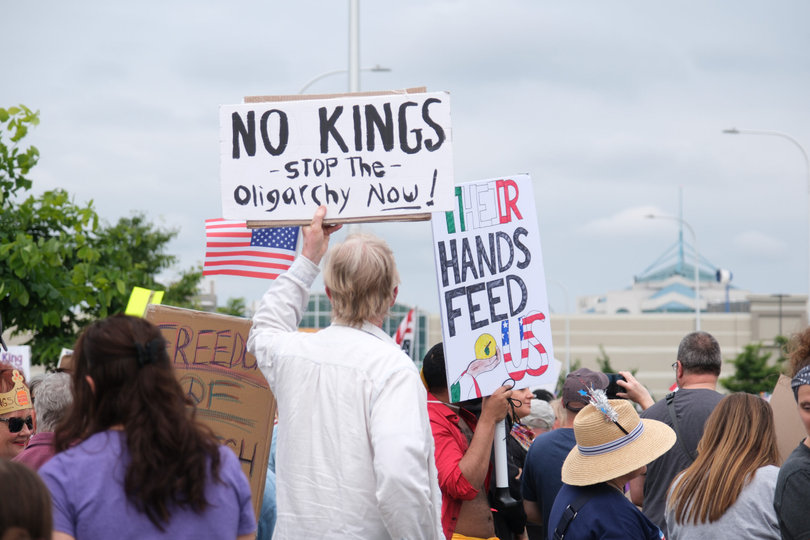 SYRACUSE, NY — Protesters hold signs criticizing President Donald Trump’s administration. Along the skyline of Destiny USA, protesters’ signs read “No Kings” and “Their hands feed us,” referring to immigrants. 
