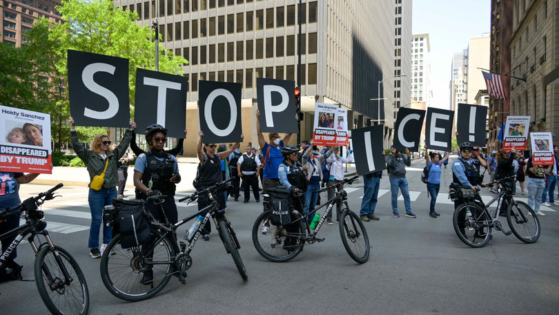 CHICAGO, IL — Protesters stand behind police officers, displaying a sign that reads “STOP ICE” in downtown Chicago. Demonstrations against ICE raids happened nationwide before the “No Kings” protests on Saturday.  