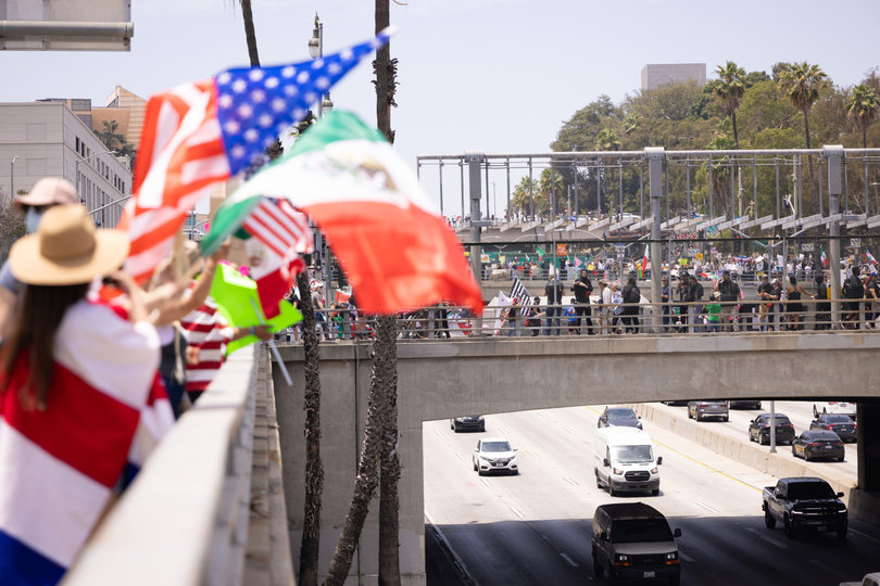 LOS ANGELES, CA — Protesters flood the streets in downtown Los Angeles, waving flags and signs, looking down at a freeway. A chorus of car honks join the shouts of demonstrators. Anti-ICE protests persisted in LA last week alongside ongoing immigration raids.