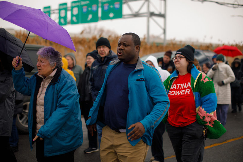 People walk, singing in front of cars in a group.