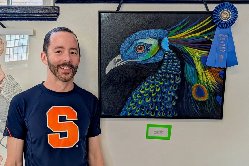 Syracuse University employee Kevin Costello stands beside his peacock painting, which won first place at the Great New York State Fair’s arts competition. Like most of his work, Costello painted the piece entirely with acrylics.