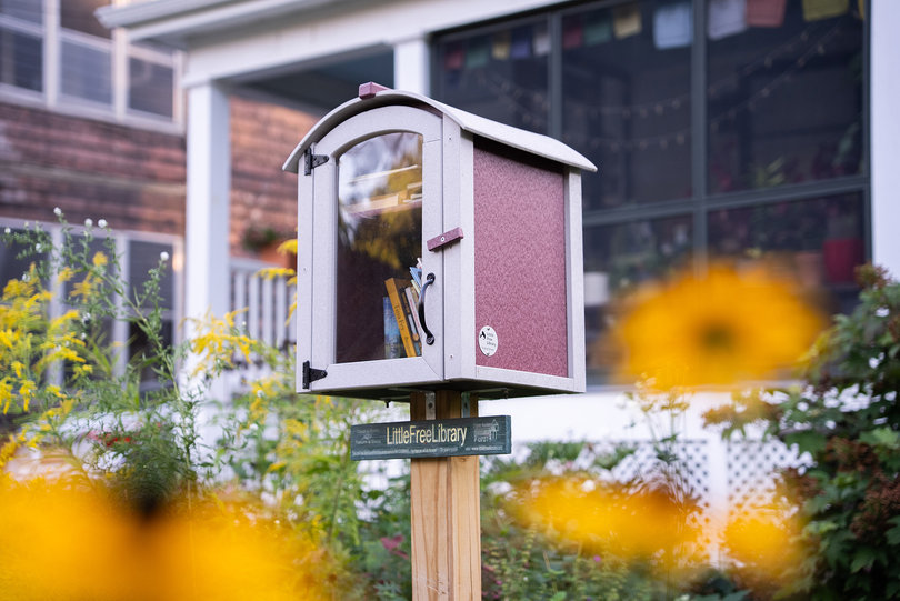 A Little Free Library box stands in a local Syracuse residential neighborhood. In between children and adult books lie pieces of fabric residents can quilt as part of the “Little Free Fibrary” initiative.