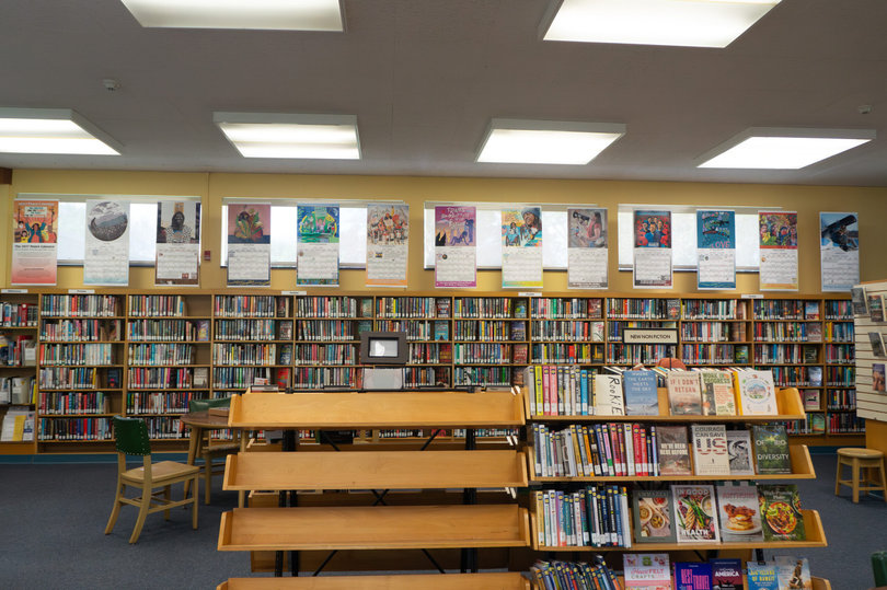 Part of "The 2027 Peace Calendar: Art to Provoke, Inspire and Offer Vision” project, 13 panels of artwork hang above bookshelves at Syracuse's Soule Branch Library. The panels also include monthly calendars with important social justice-related dates from the past.