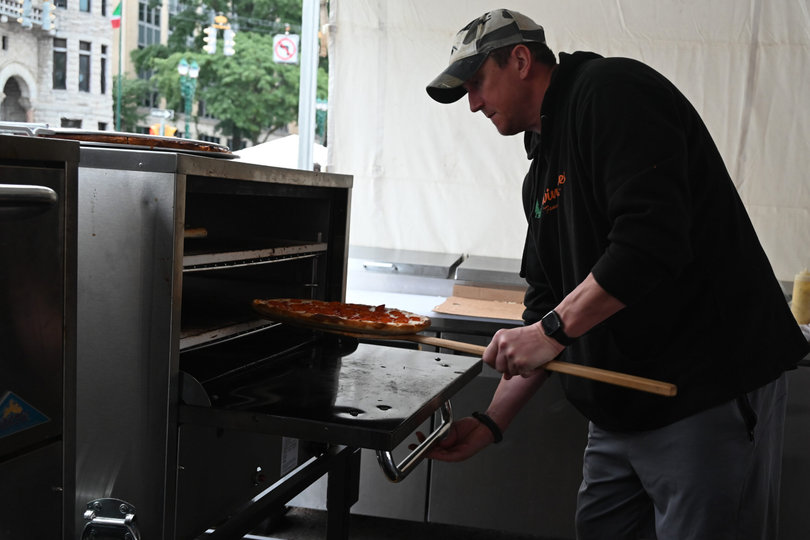 A Festa Italiana volunteer cooks a pepperoni-filled pizza in a food booth. Pizza, zeppole and tiramisus are among the foods available at Festa Italiana.
