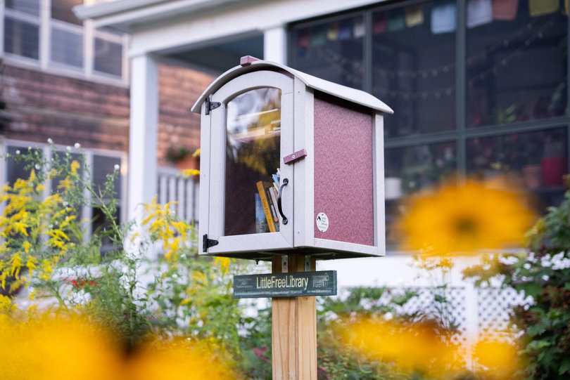 A Little Free Library rests among flowers in a Syracuse-area neighborhood. Since June, locals have taken pieces of fabric from 11 of the libraries to be sewn into a community quilt.